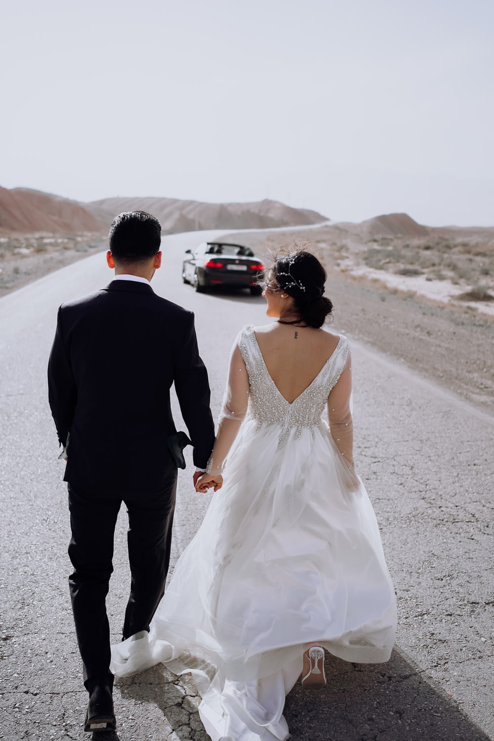 a bride and groom walking down the road holding hands