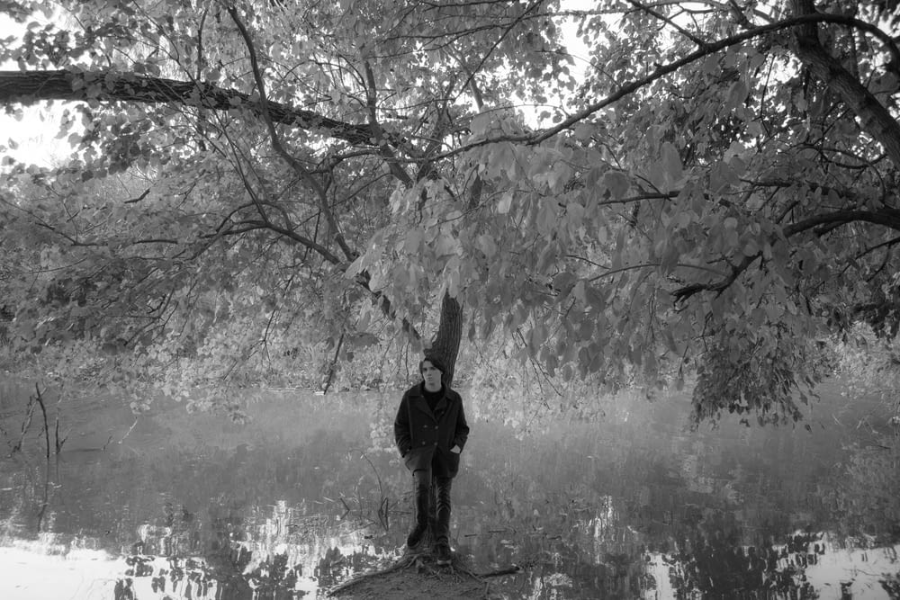 a black and white photo of a person standing next to a tree