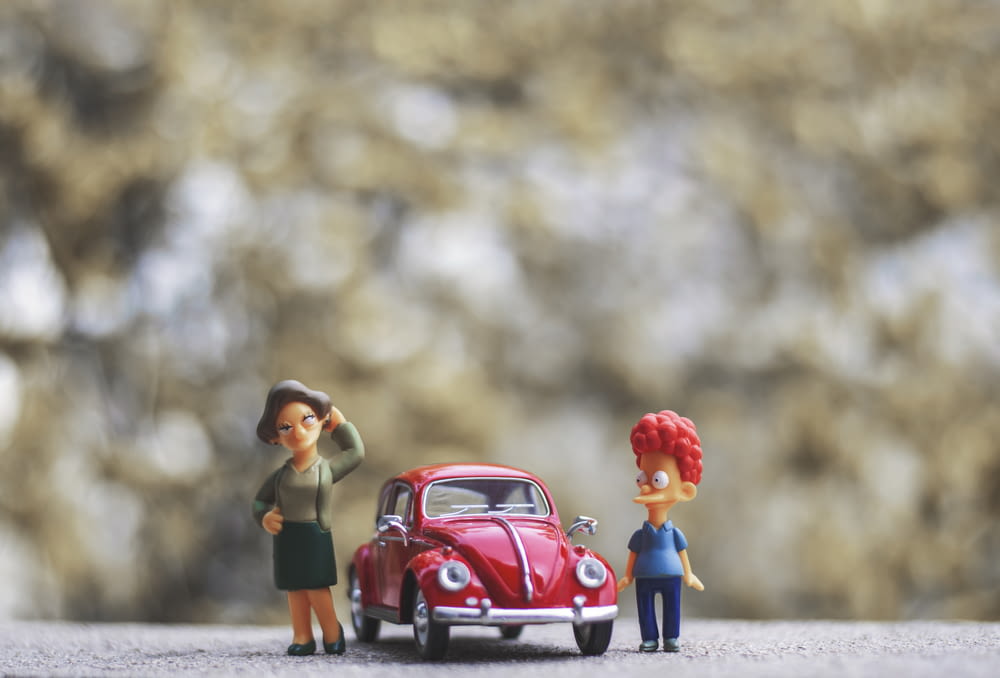 Ein paar Figuren stehen neben einem roten Auto