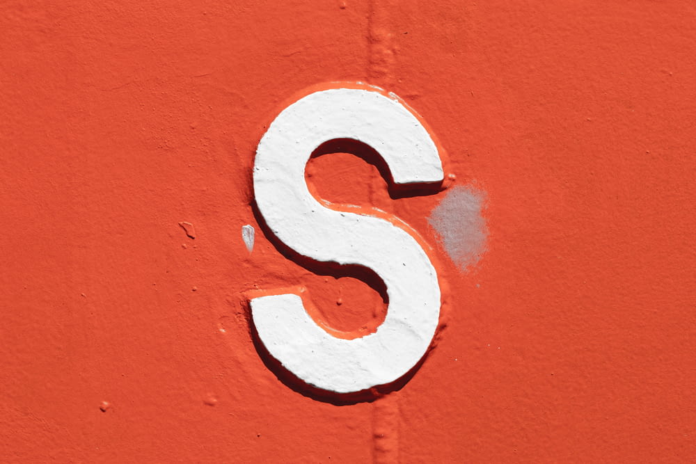 a close up of a white letter s on an orange wall