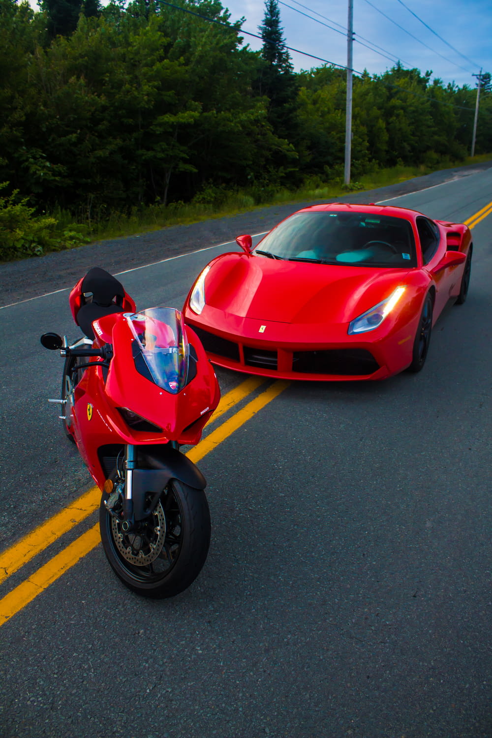 a red sports car and a red motorcycle on a road