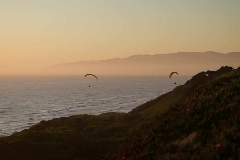 a couple of paraglides flying over the ocean at sunset