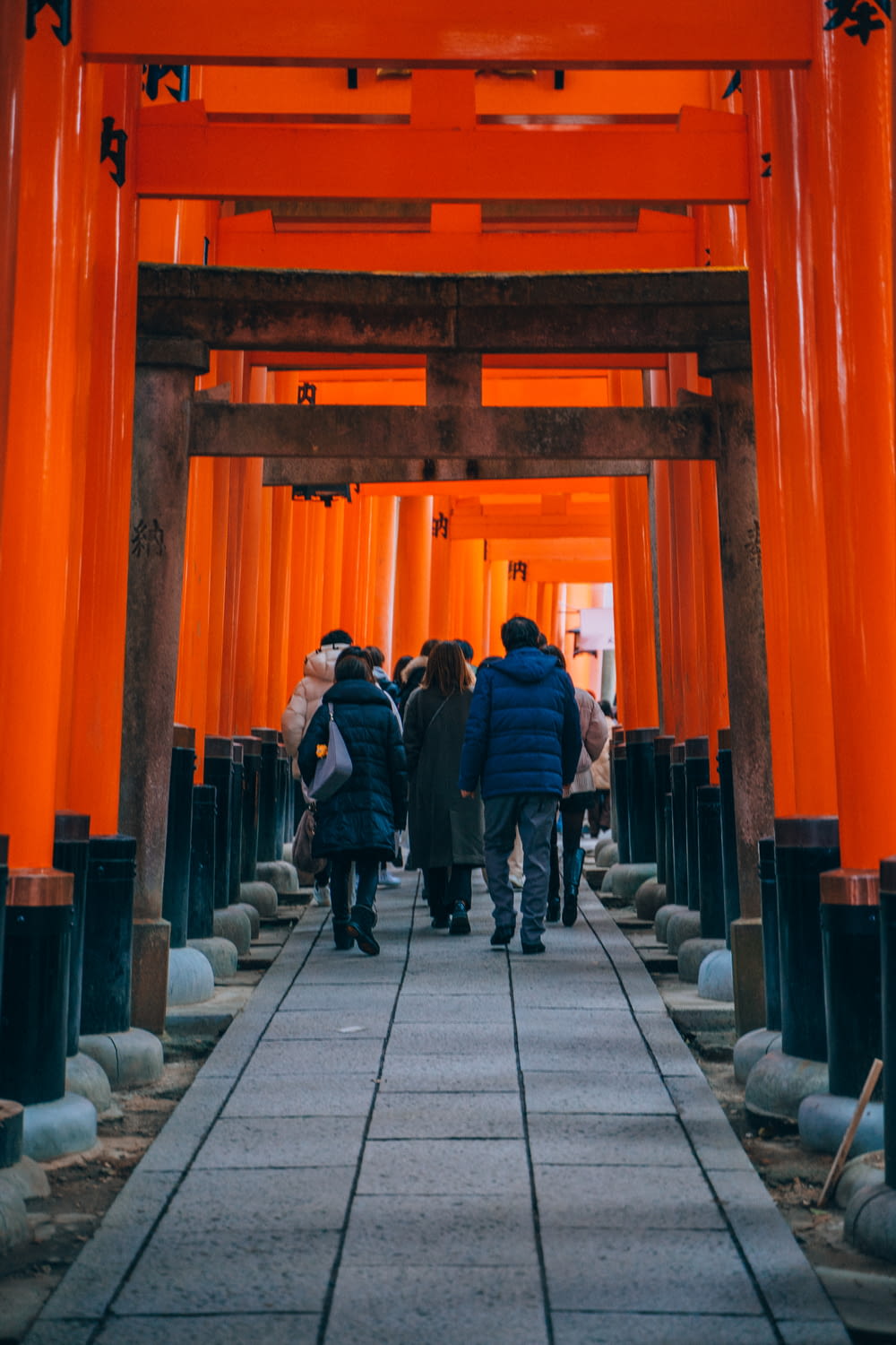 a group of people walking under a tall orange structure