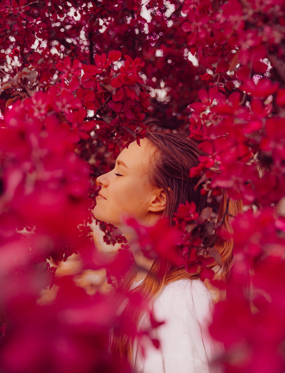 a woman is standing under a tree with red leaves