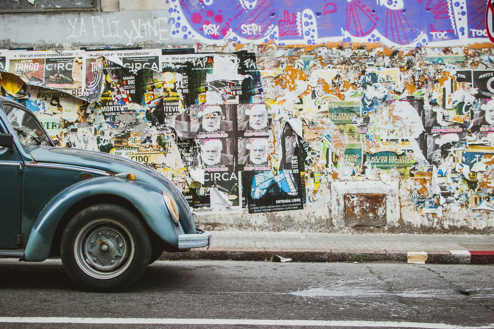 a blue car parked in front of a wall covered in graffiti