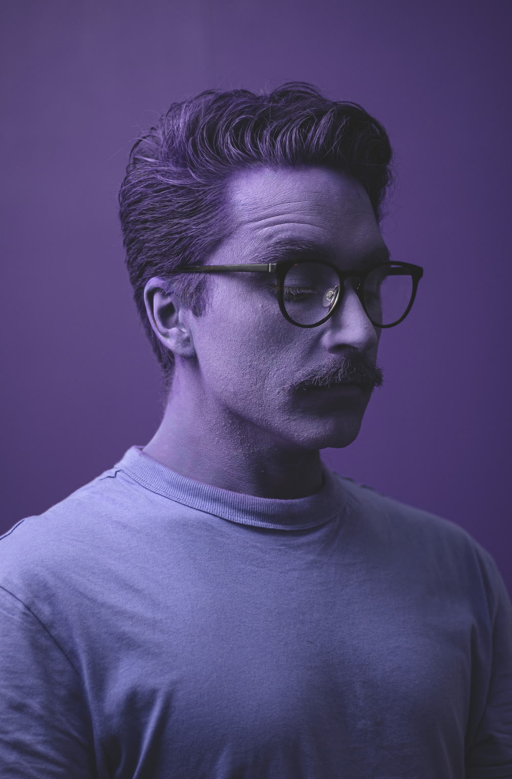 a man with a mustache and glasses on a purple background