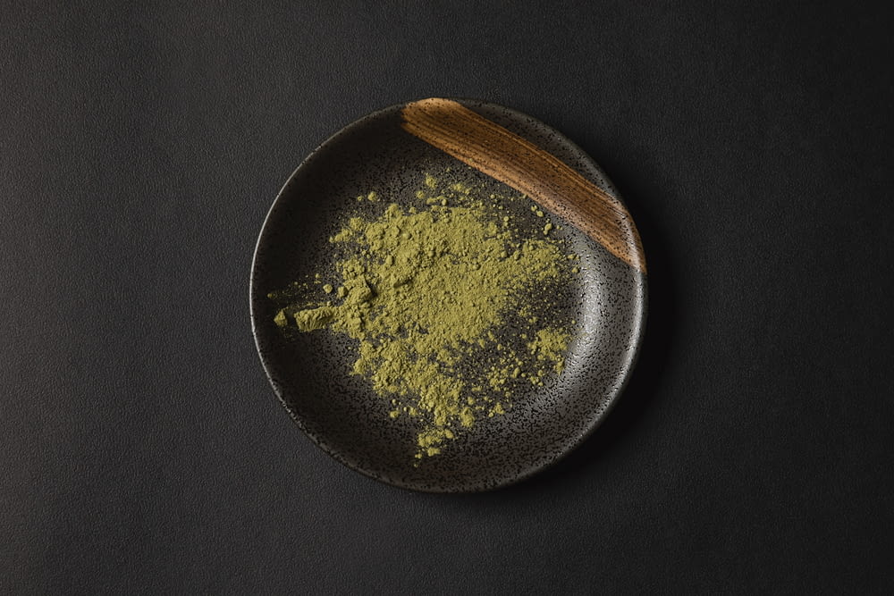 a black plate topped with green powder and a wooden spoon