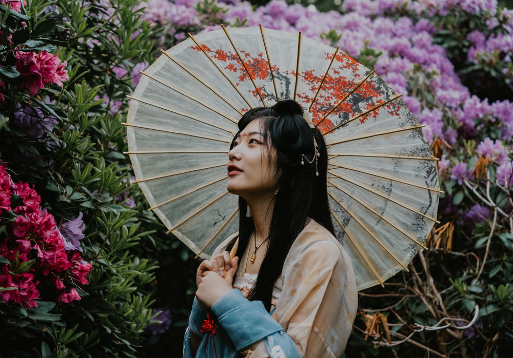 a woman standing in front of flowers holding an umbrella
