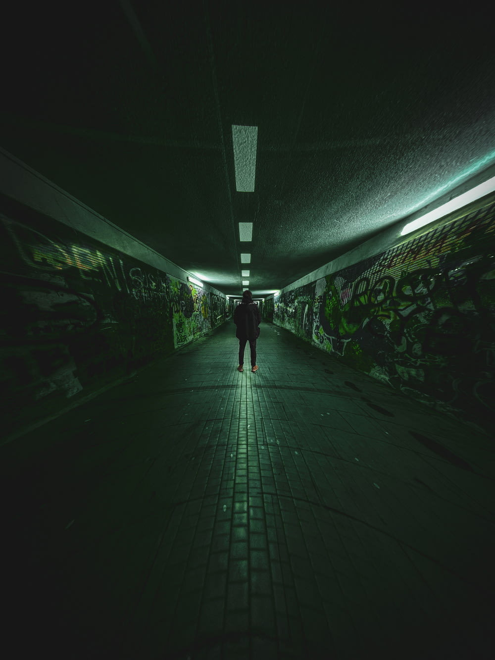 a person walking down a dark tunnel with graffiti on the walls