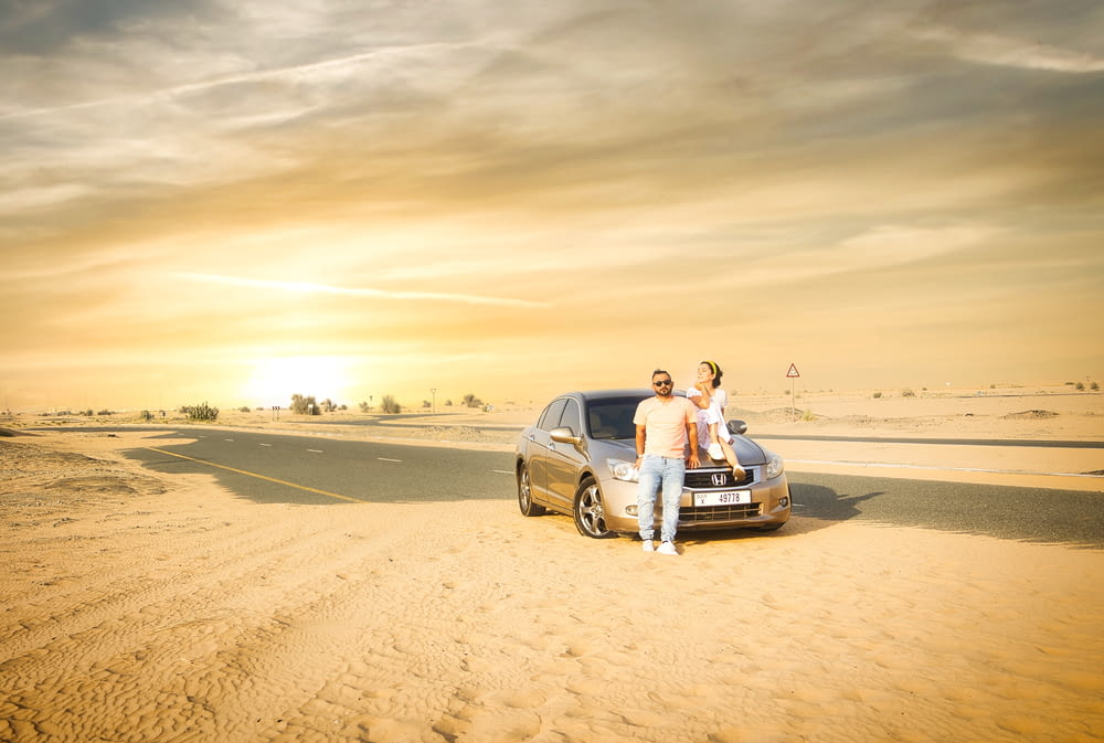 a man and woman standing next to a car in the desert
