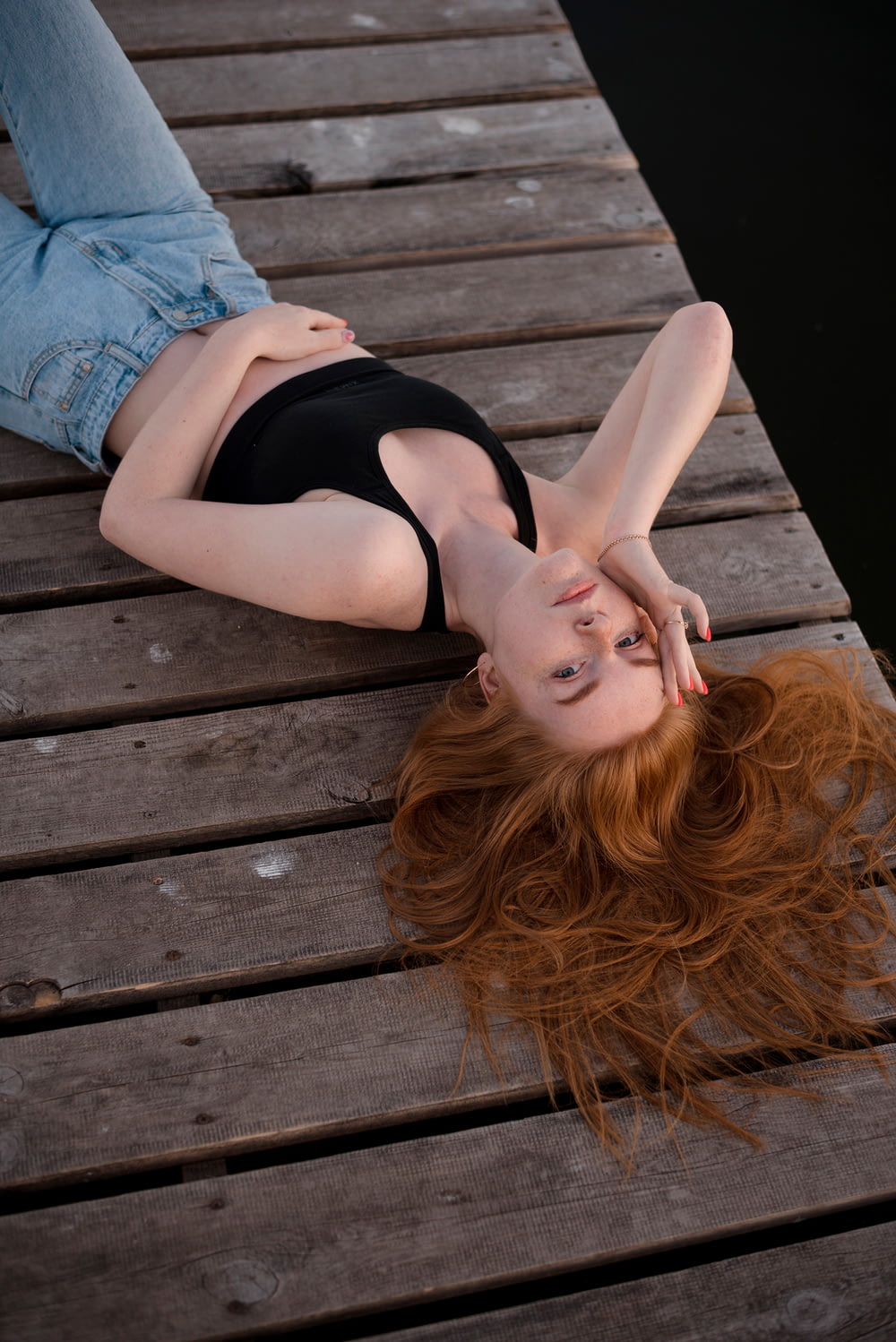 a woman with red hair laying on a dock