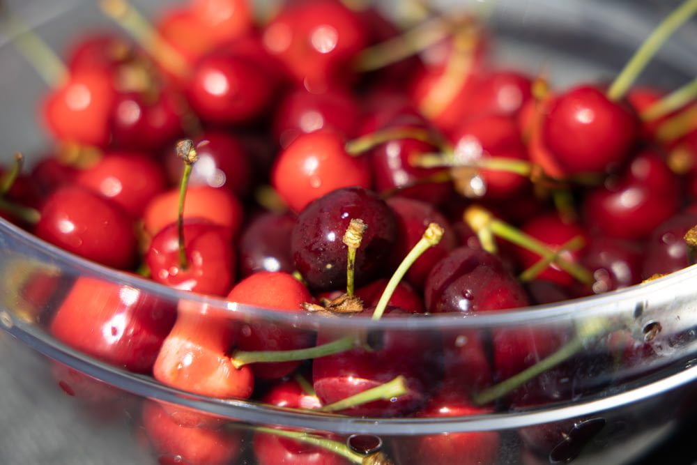 a glass bowl filled with cherries on top of a table