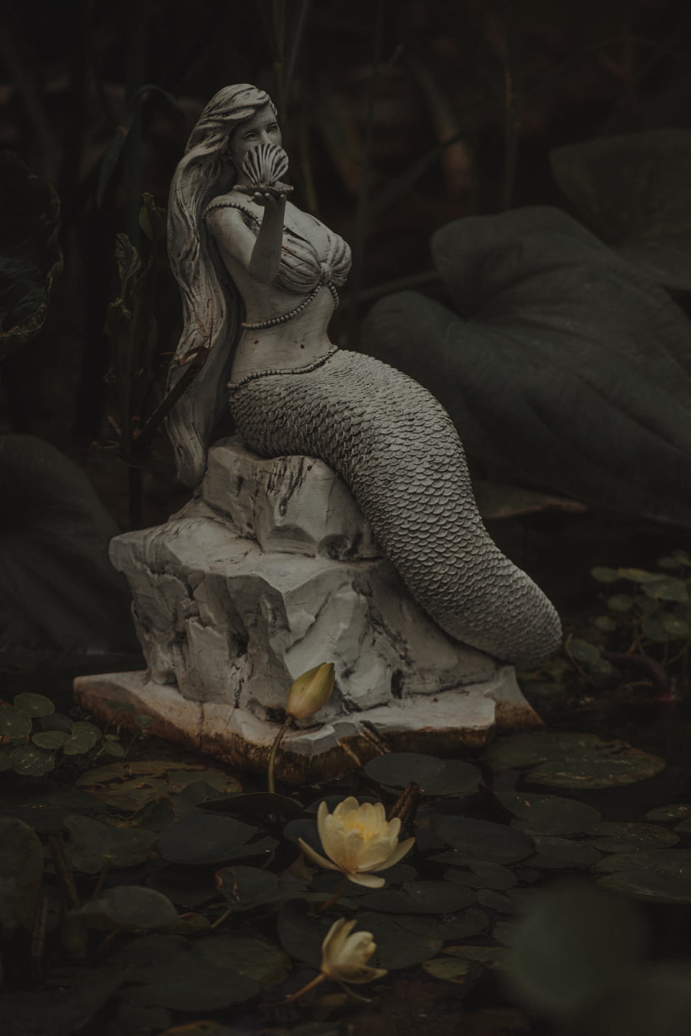 a statue of a person sitting on a rock in a pond