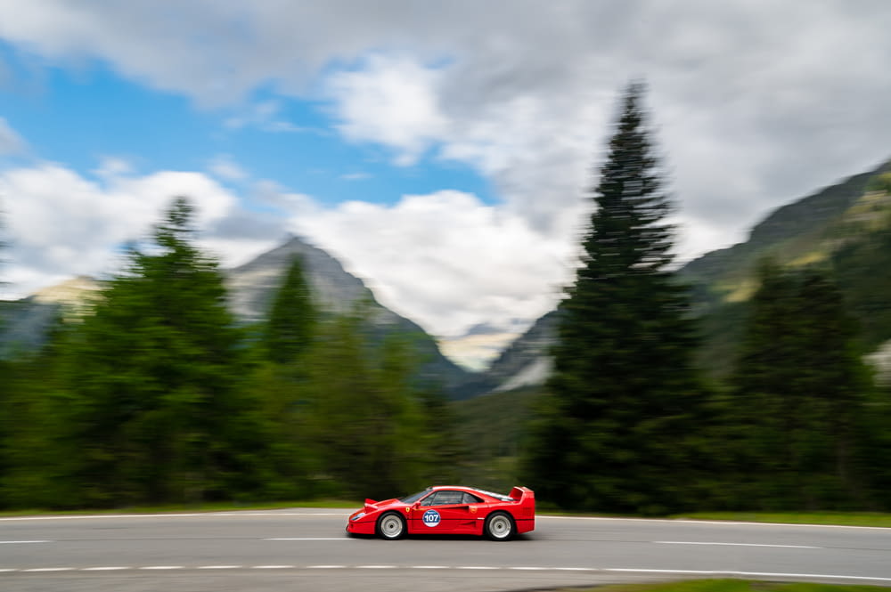 a red sports car driving on a road with trees and mountains in the background