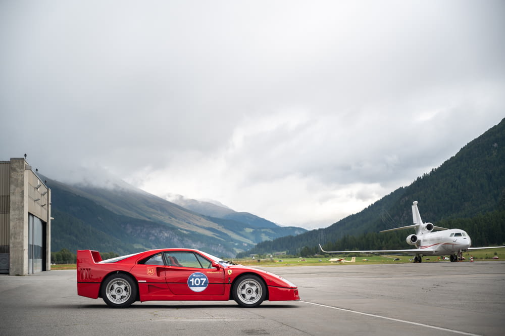 a red sports car parked next to a plane on a runway