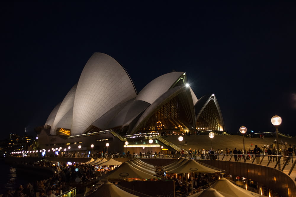 a large building with a crowd of people in front of it with Sydney Opera House in the background