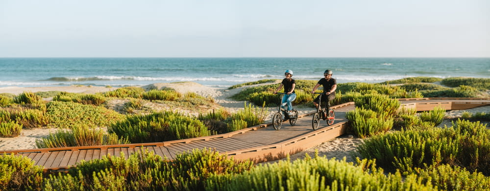 two people riding bikes on a boardwalk