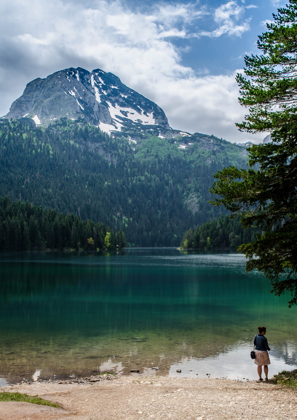 a person standing next to a lake with a mountain in the background