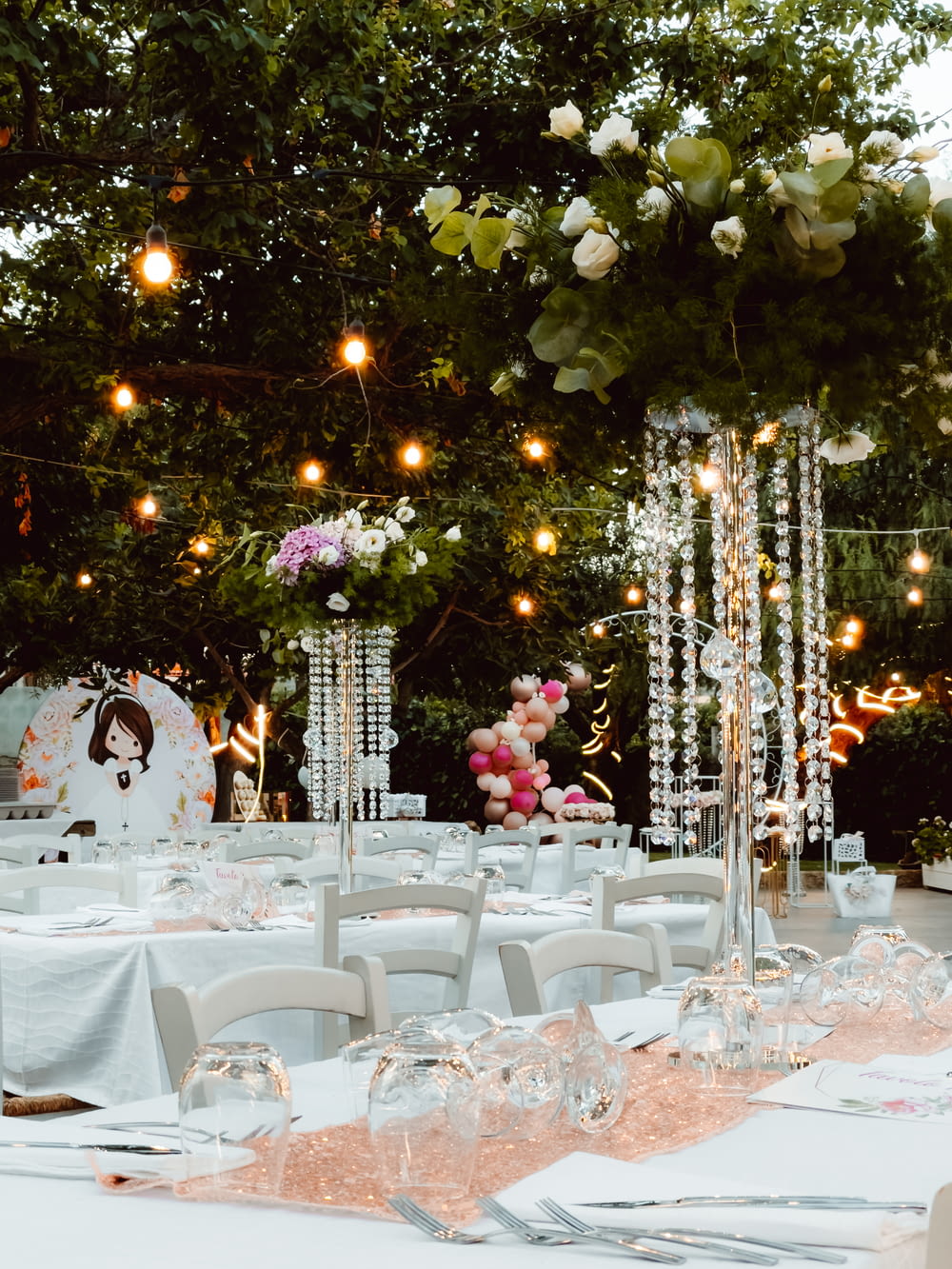 a table with white tables and chairs under a tree with lights