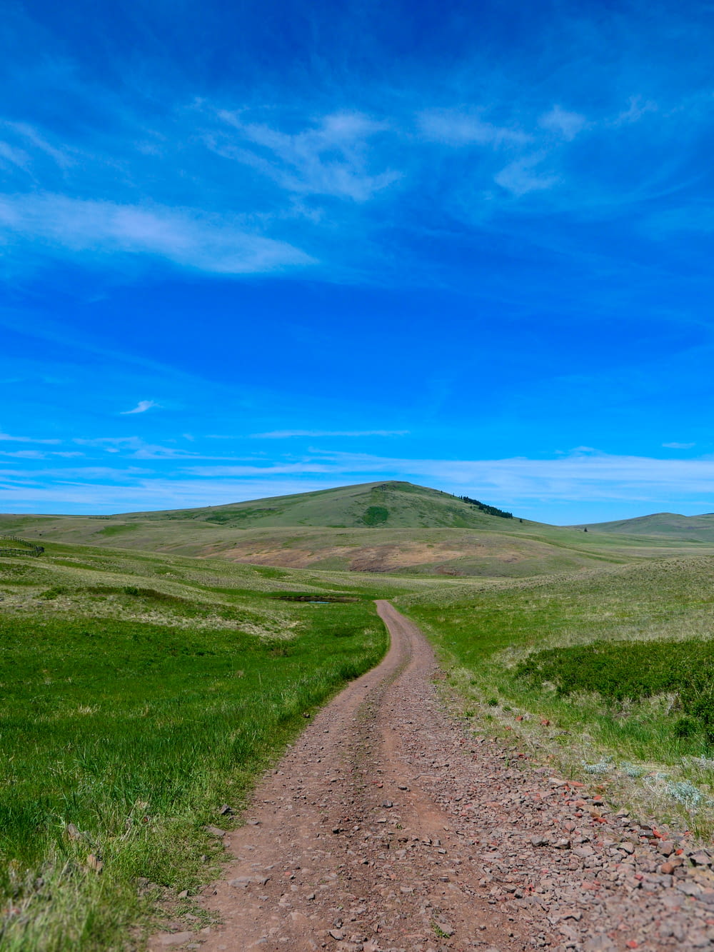 a dirt road leading up to a hill with a grassy hill in the background