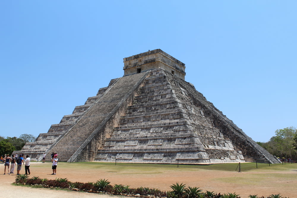a pyramid with people standing in front of it with Chichen Itza in the background