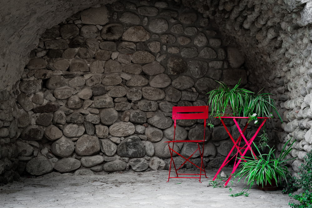a red chair and a plant in front of a stone wall