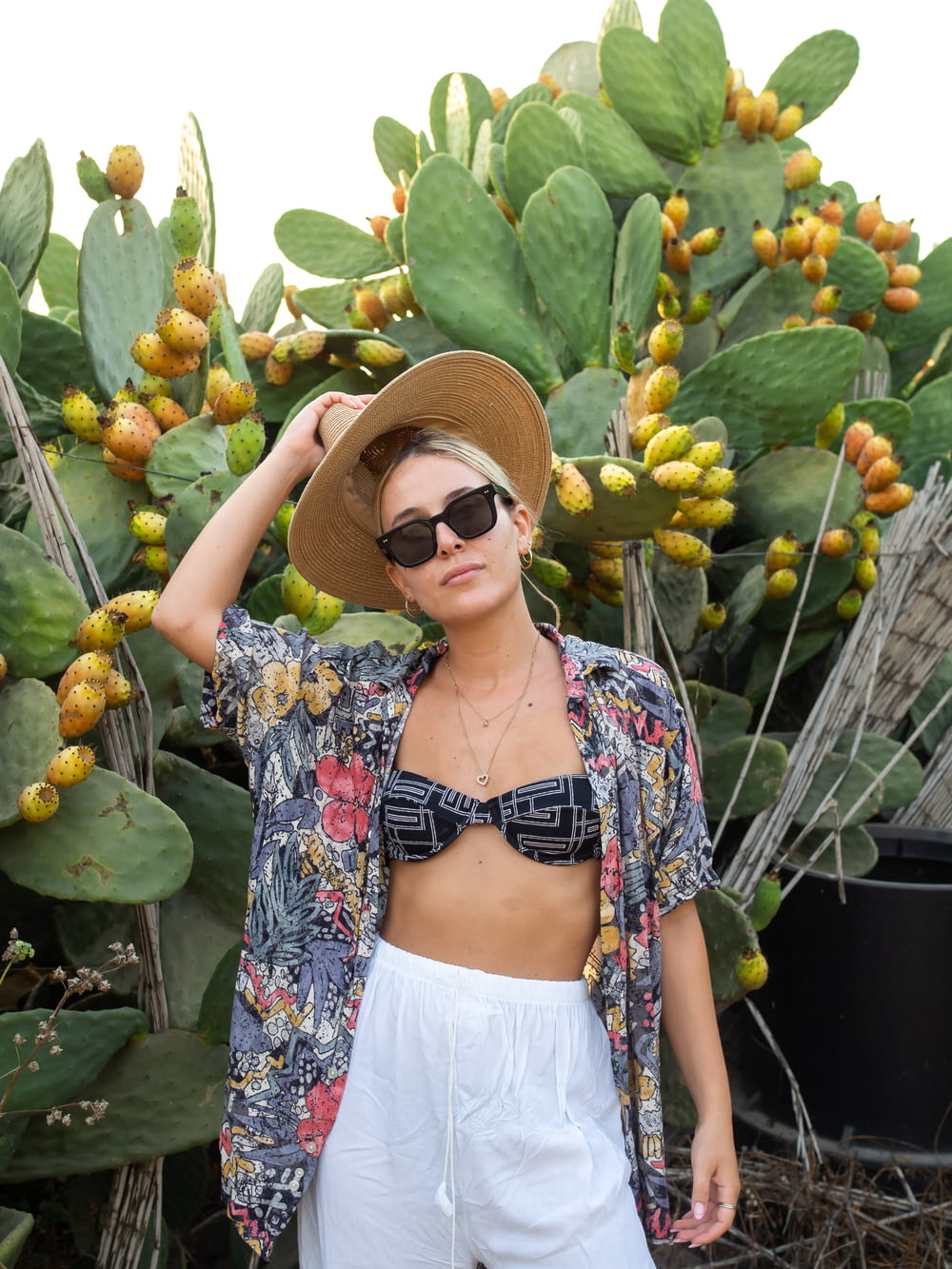 a person wearing a hat and sunglasses standing in front of a bunch of fruit