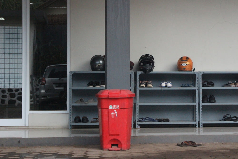 eine rote Mülltonne neben einem Regal mit Gegenständen darauf