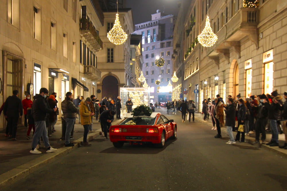 a red sports car on a street with people walking around