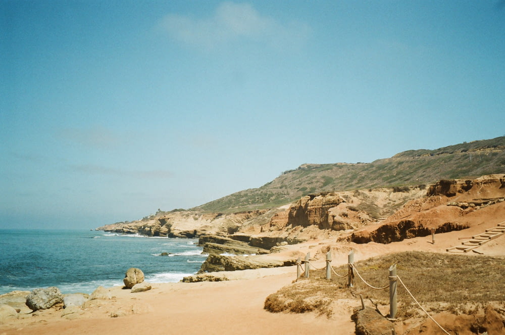 a beach with a fence and a hill with a body of water