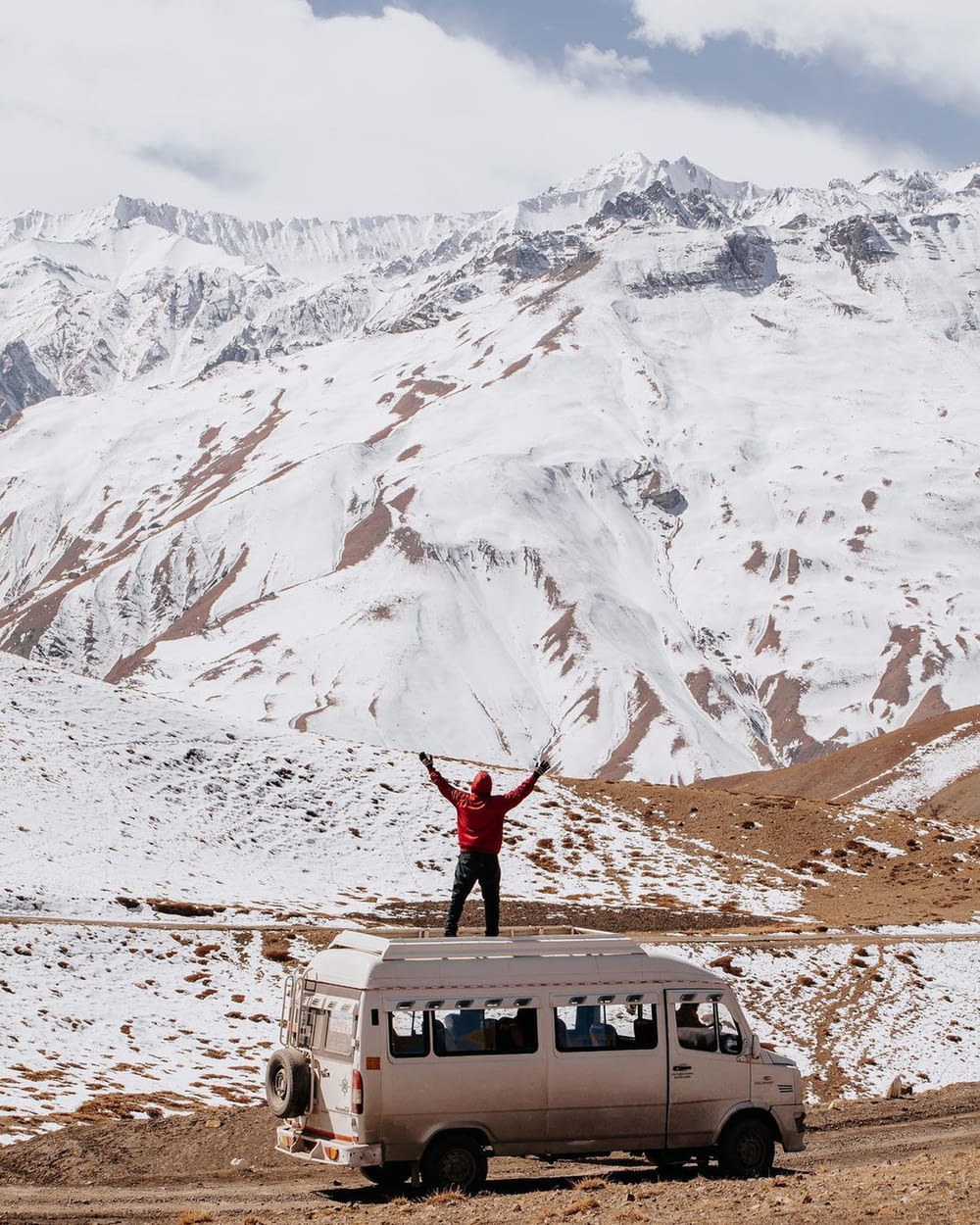 a man standing on a van in front of a mountain