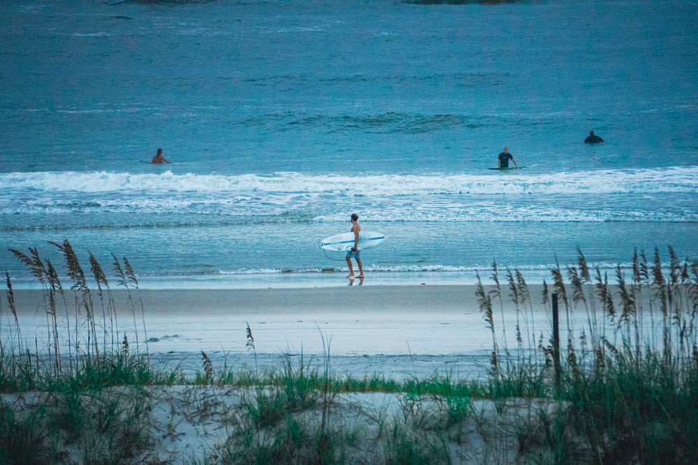 a couple of people walk across the beach with surfboards