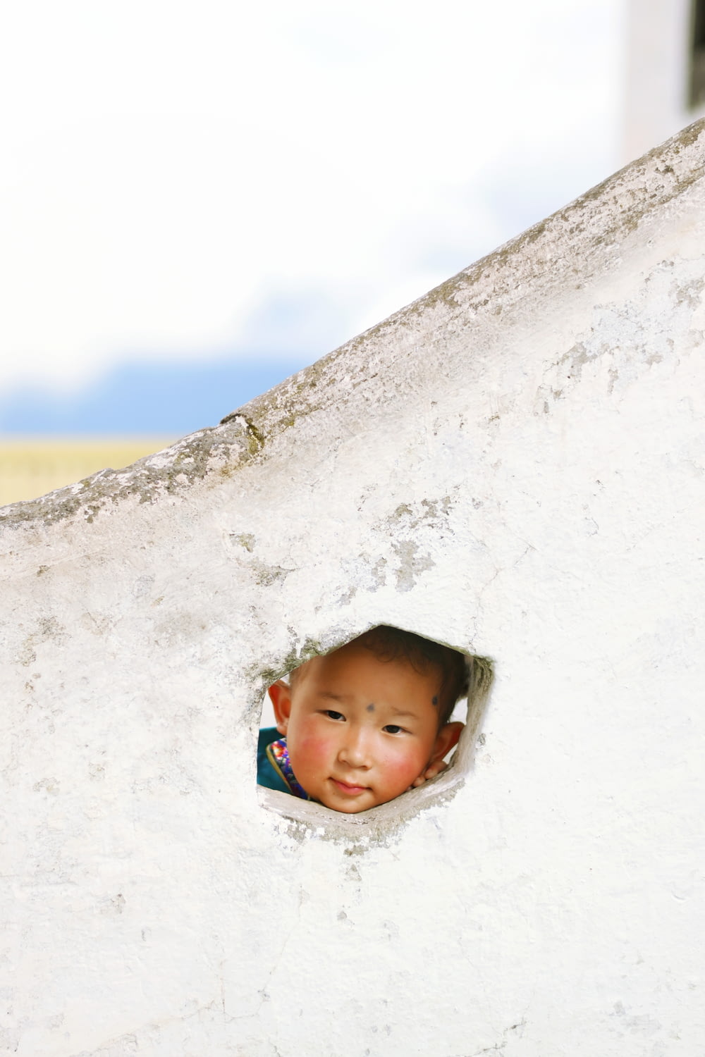 a boy peeking out of a hole in a wall