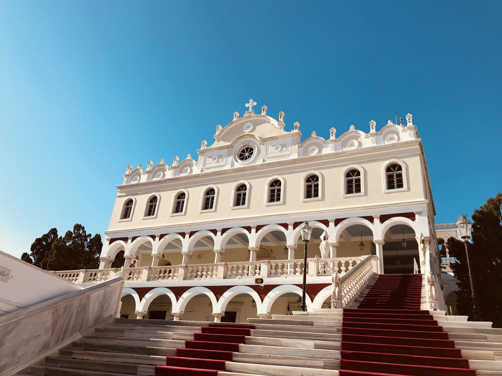 a large white building with red stairs with Tinos in the background
