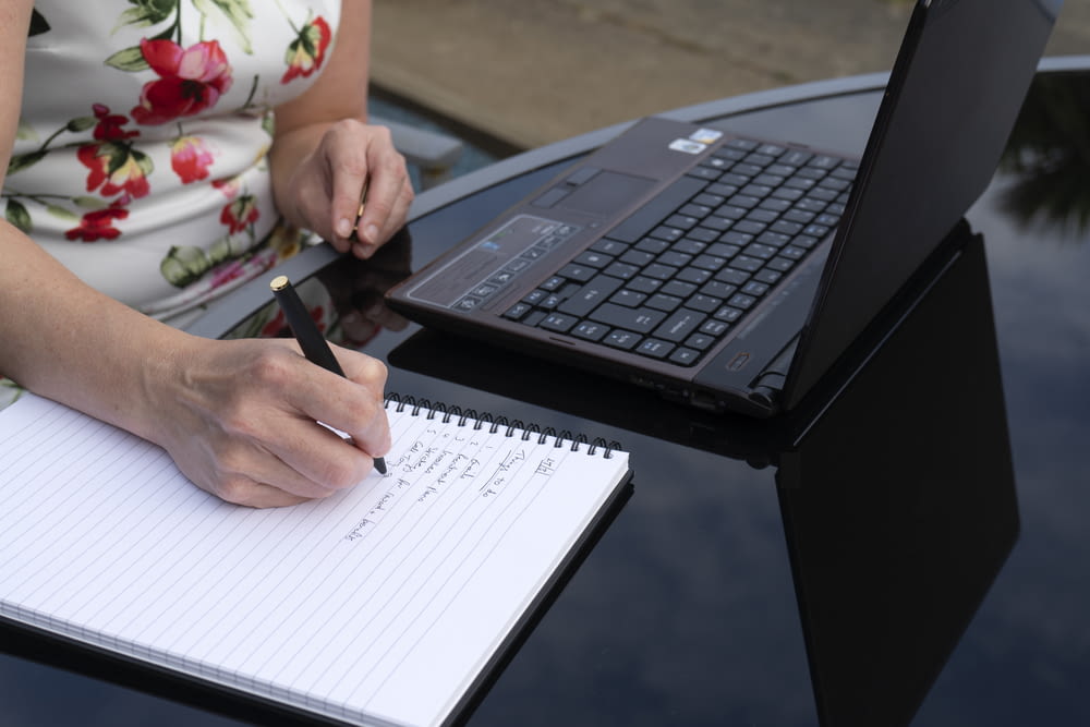 a person writing on a piece of paper next to a laptop