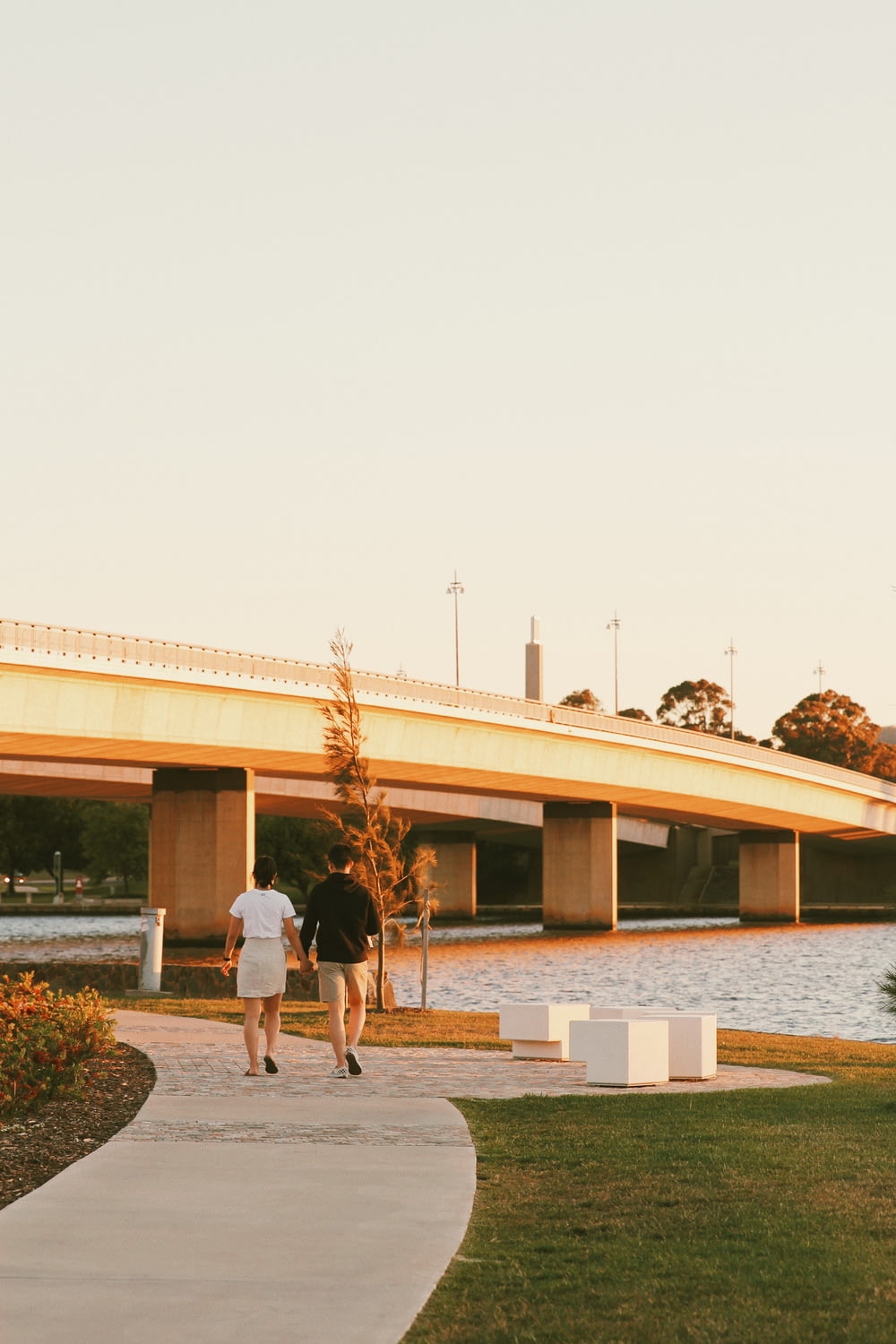 a couple of people walking on a path by a building with a bridge