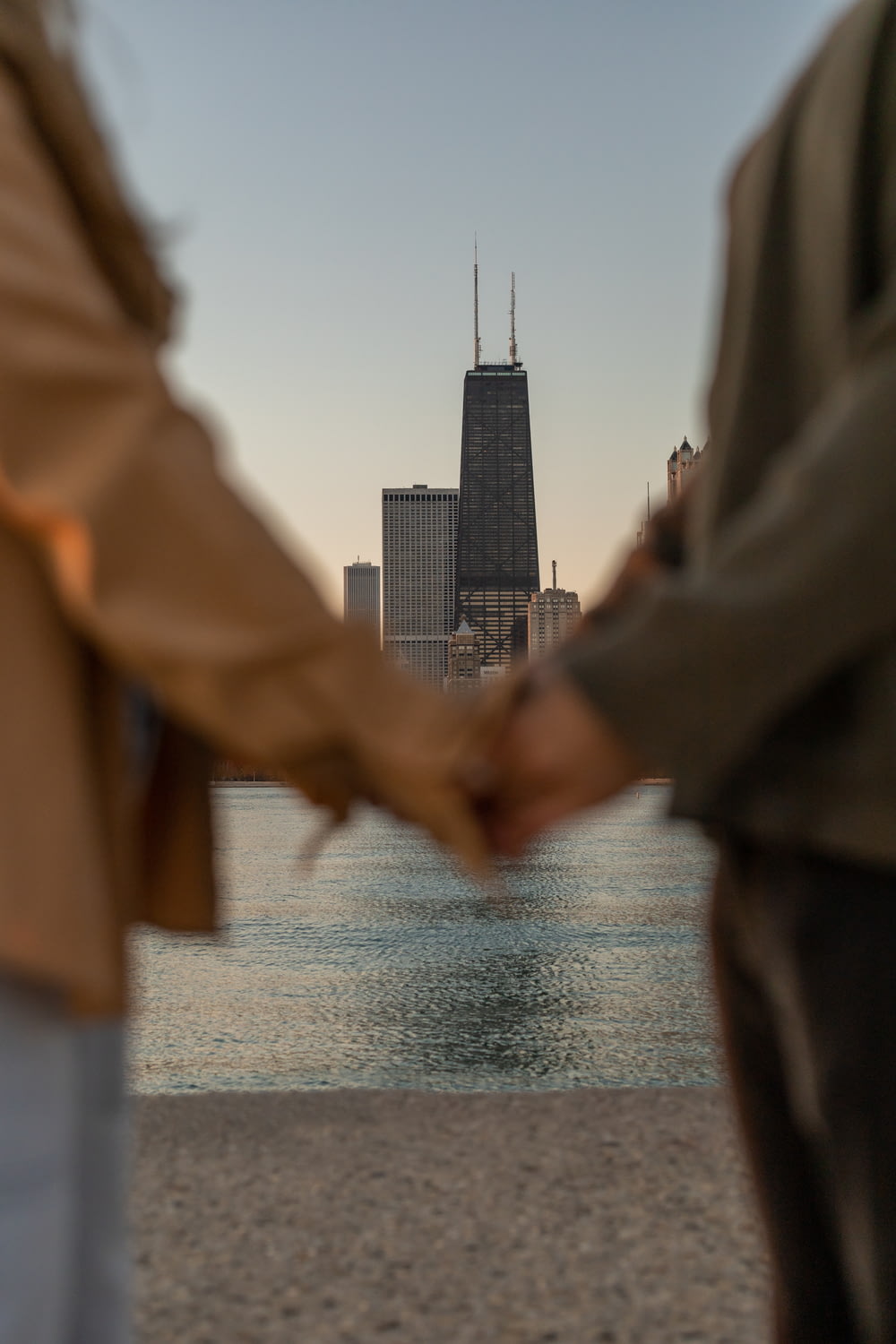 a person holding their hand up to a body of water with a tall building in the background