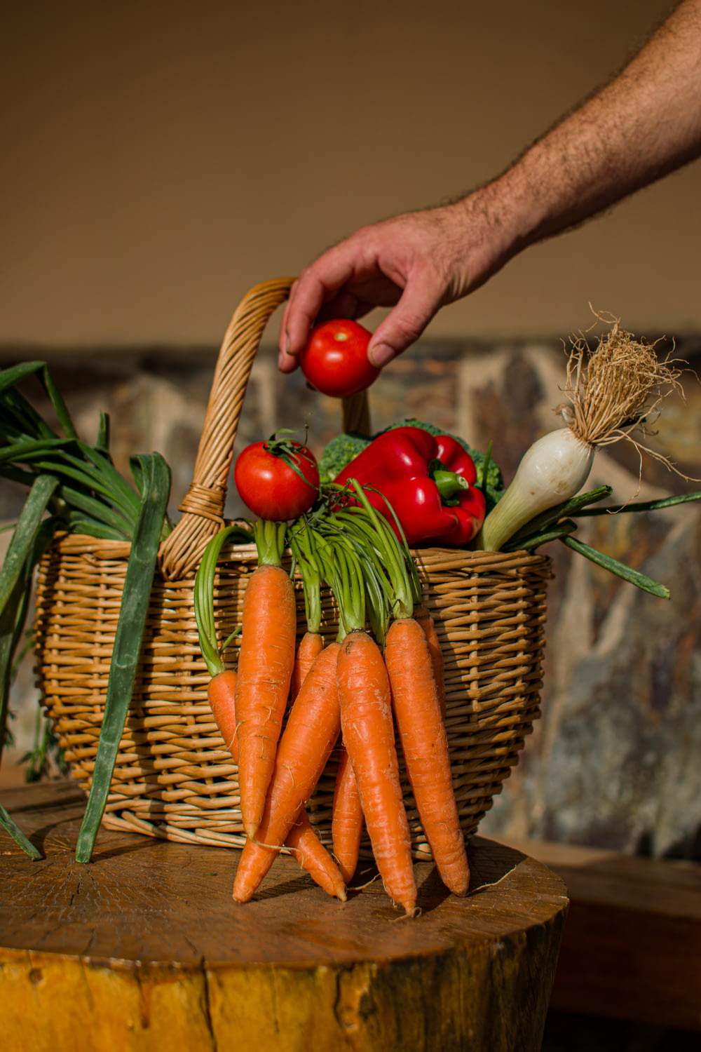 a hand holding a carrot over a basket of vegetables