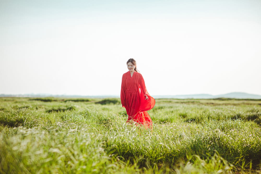 a person in a red dress standing in a field of grass
