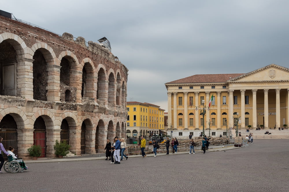 um grupo de pessoas andando em torno de um pátio com edifícios ao fundo com Verona ao fundo