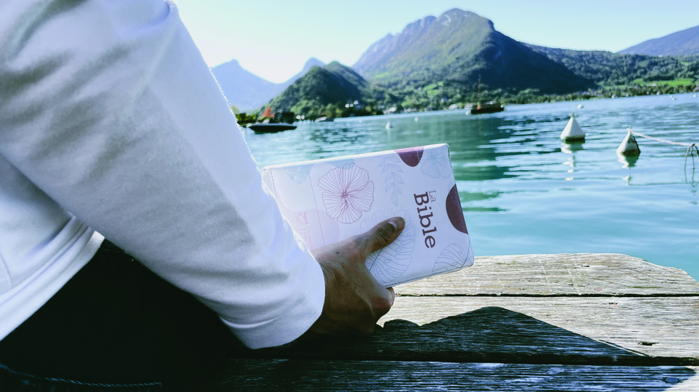 a hand holding a white paper bag over water with mountains in the background