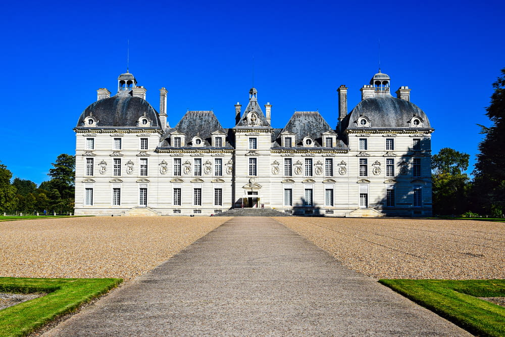 a large white building with a road in front of it with Château de Cheverny in the background