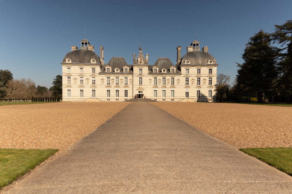 a large white building with a lawn and trees in front of it with Château de Cheverny in the background