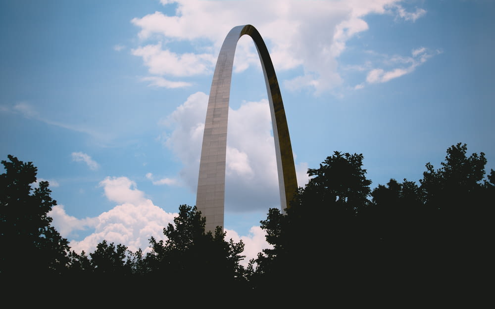 a tall monument with trees in front of it with Gateway Arch in the background