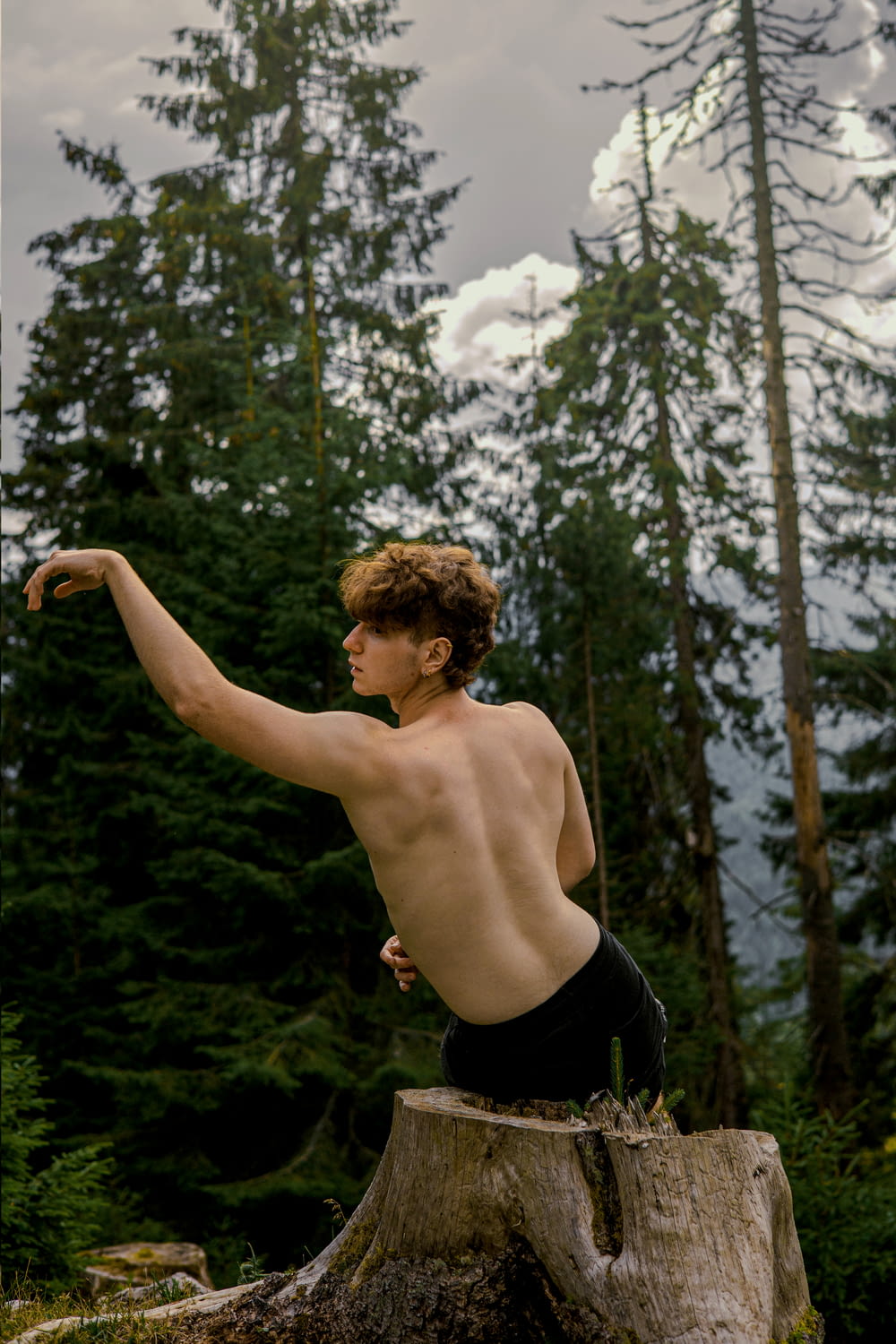 a shirtless man posing on a rock in the woods