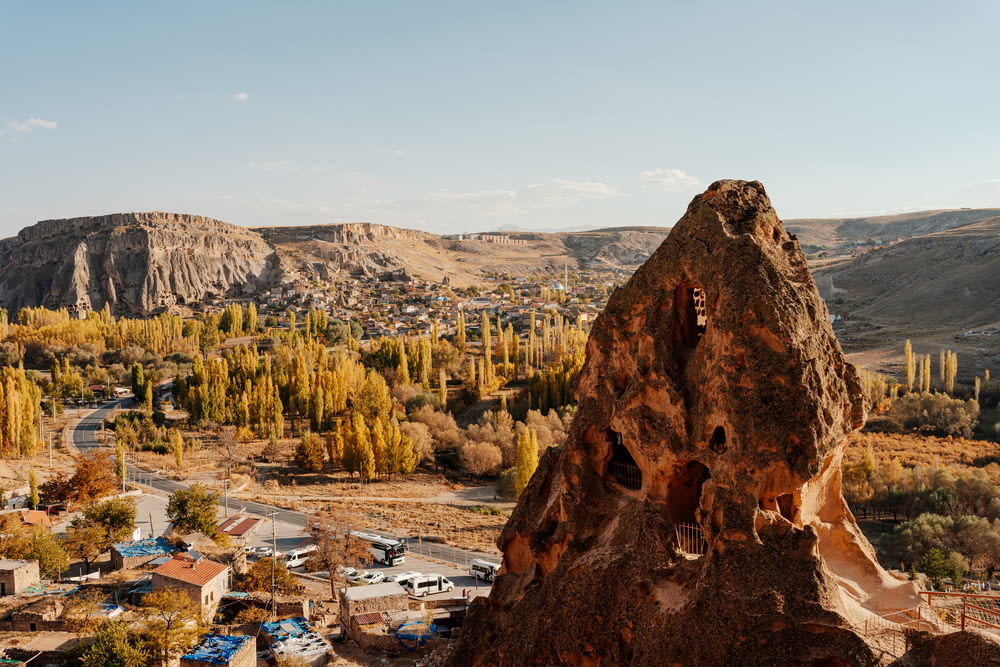 a large rock formation with a town below it with Cappadocia in the background