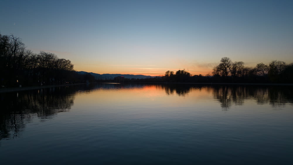a body of water with trees and a sunset in the background
