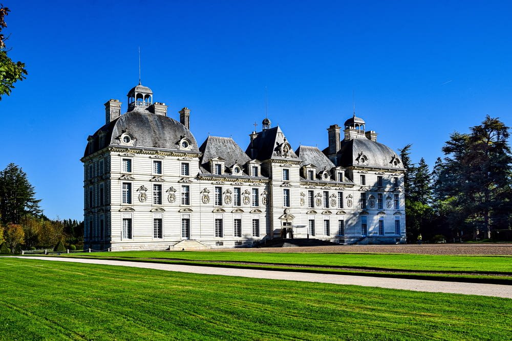 a large white building with a lawn in front of it with Château de Cheverny in the background