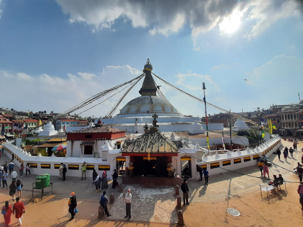 a group of people walking around a large building with a domed roof with Boudhanath in the background