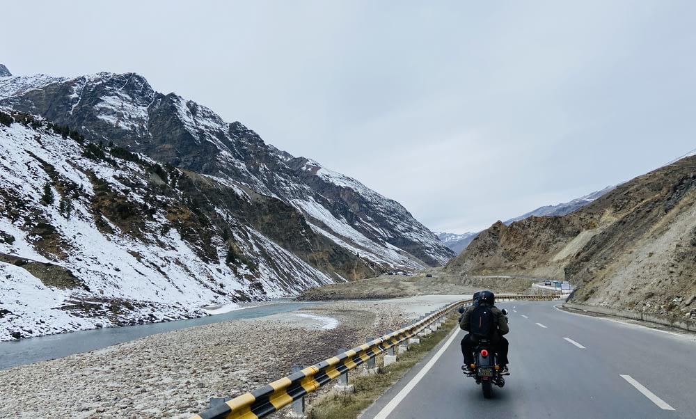 um homem andando de moto por uma estrada ao lado de uma montanha